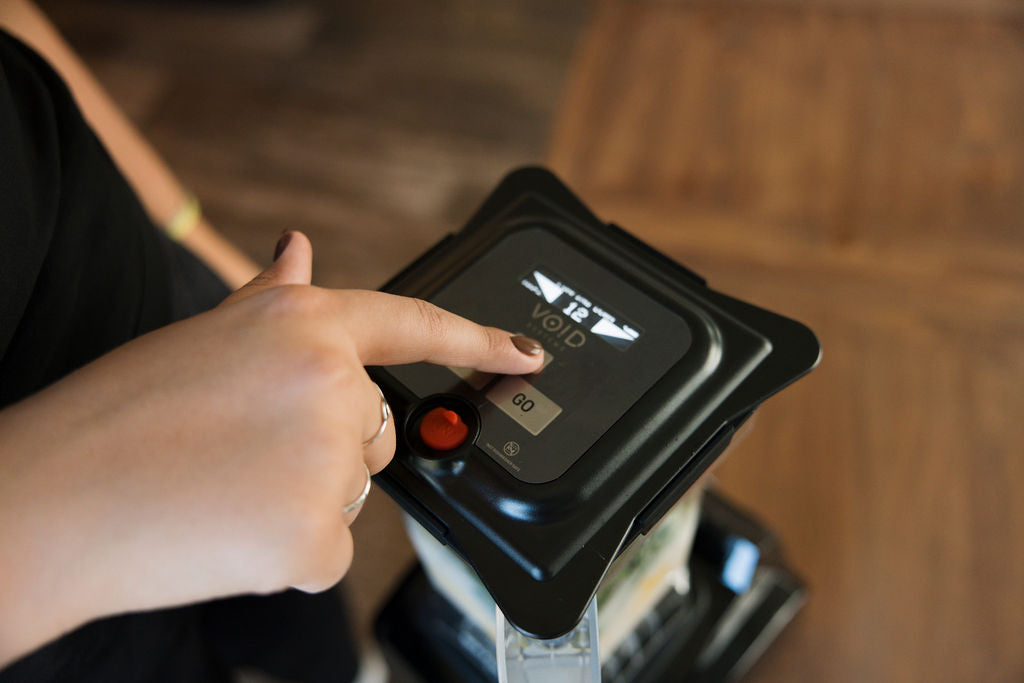A finger pressing the Go button on a VOID lid seated on a blender jar