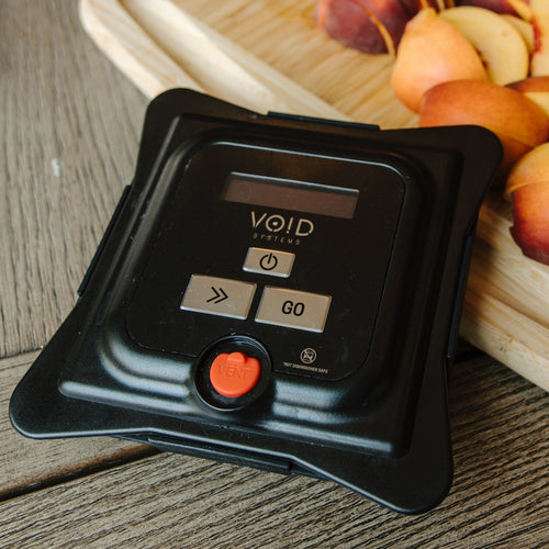 The VOID vacuum lid on a wooden counter next to a cutting board of sliced peaches